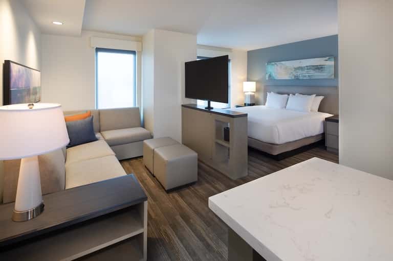 Modern hotel suite with queen bed, sofa, flat-screen TV, and contemporary furnishings