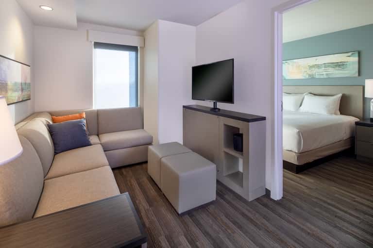 Suite interior with living area sofa, TV, bedroom with queen bed, and modern furnishings