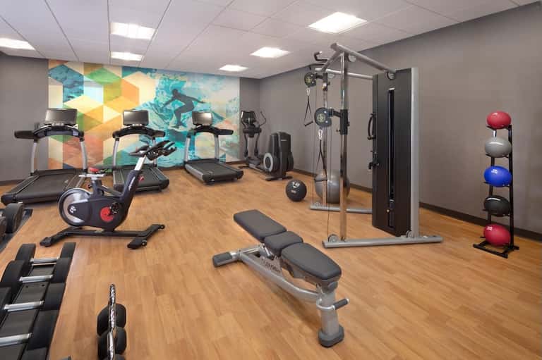 Hotel fitness center with exercise bikes, strength training equipment, and colorful wall mural