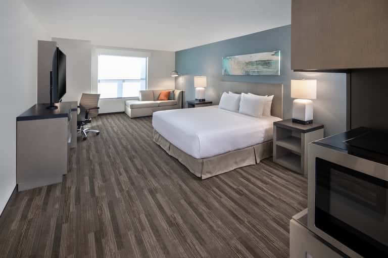 Modern hotel room with queen bed, seating area, flat-screen TV, and blue accent wall