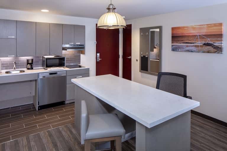 Modern kitchenette in suite with gray cabinetry, stainless steel appliances, white countertop, and dining area