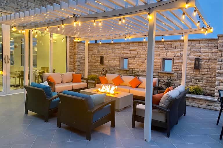 Illuminated patio pergola with fireplace, comfortable seating, and ambient lighting