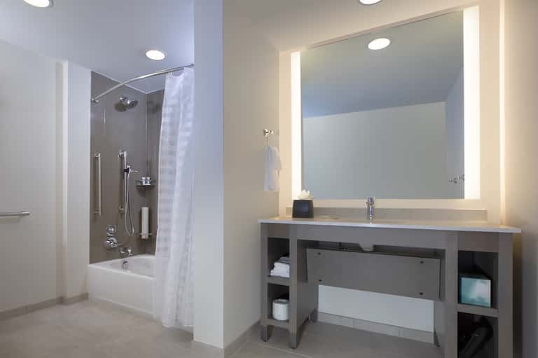 Modern bathroom vanity with illuminated mirror, storage cabinets, and adjacent shower enclosure