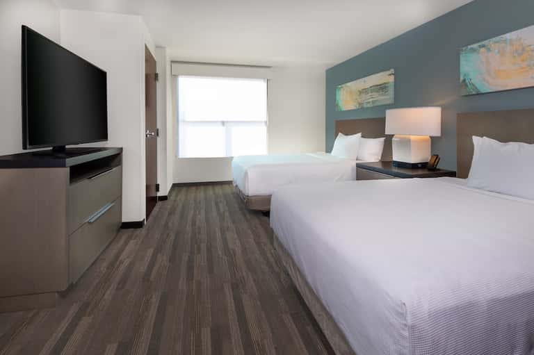 Modern hotel guest room with two queen beds, blue accent wall, and flat-screen TV