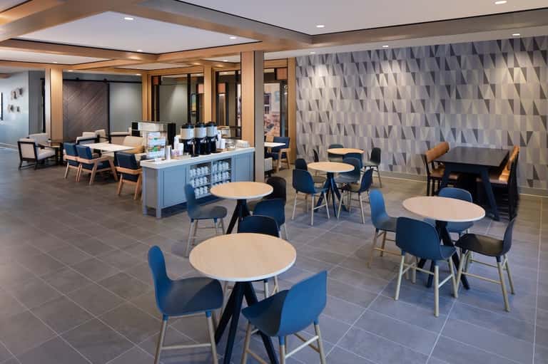 Modern hotel lobby café with round tables, blue chairs, service counter, and geometric wall patterns