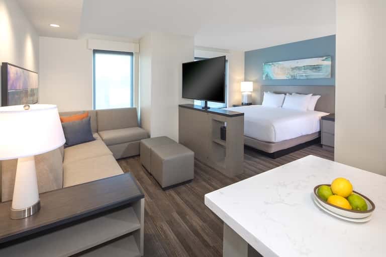 Modern hotel suite with bed, living area, flat-screen TV, and contemporary furnishings