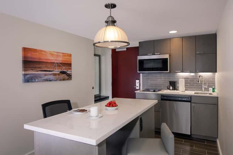 Modern kitchen and dining area with white island, stainless appliances, pendant light, and coastal artwork