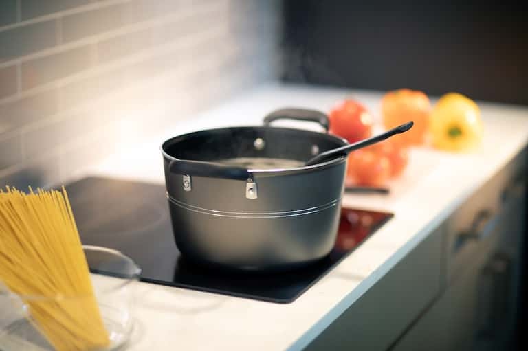 Kitchen stovetop with black cookware, pasta, and fresh vegetables in bright natural light