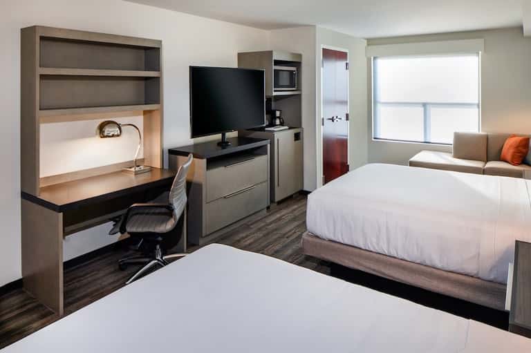 Hotel room with two beds, desk workspace, TV, kitchenette, and seating area