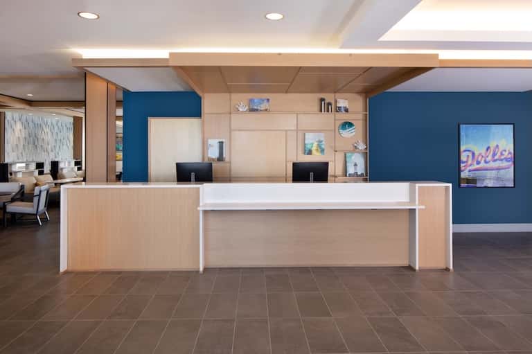 Contemporary hotel reception desk with wood paneling, blue accent walls, and neon signage