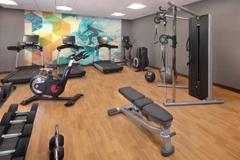 Modern hotel fitness center with treadmills, exercise bike, weights, colorful mural, and strength equipment