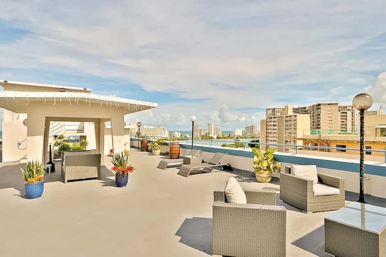 Rooftop terrace with rattan furniture, water views, modern pergola, and urban skyline in the background