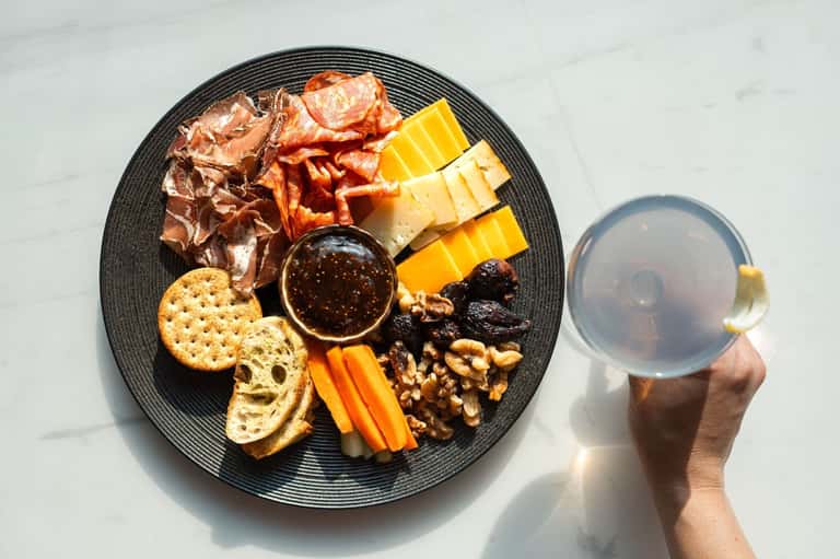 Charcuterie board with cured meats, cheese, crackers, nuts, and dip with beverage