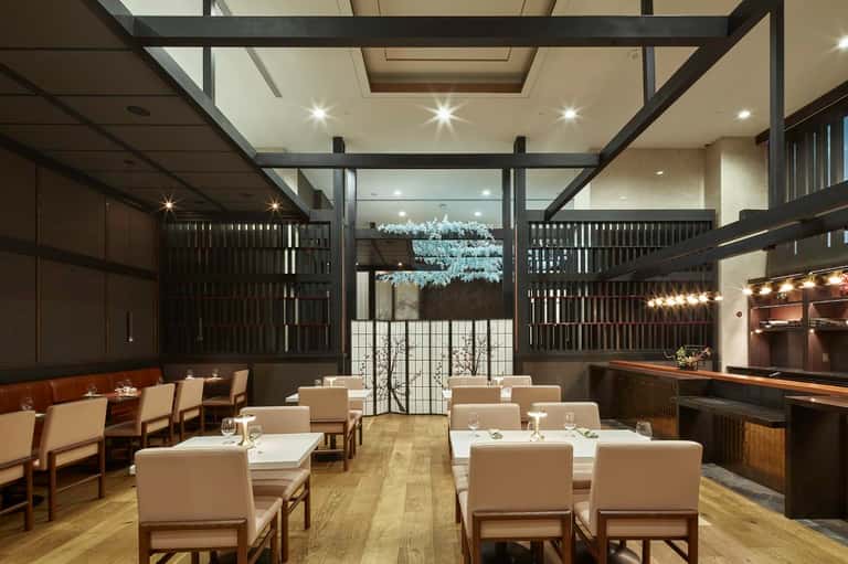 Modern fine dining restaurant with dark wooden beams, cream chairs, and illuminated bar