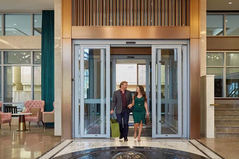 Hotel lobby entrance with couple walking through glass doors, marble floors, and modern fixtures