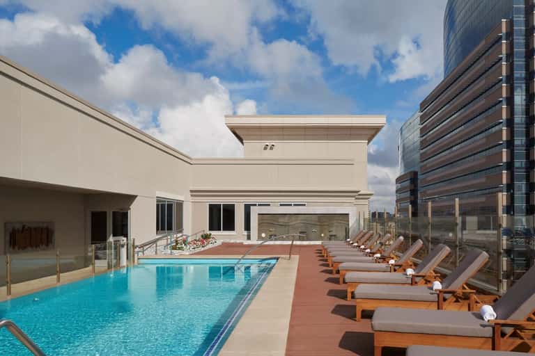 Rooftop pool deck with lounge chairs, ocean city skyline views, and modern architecture