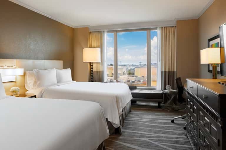 Hotel bedroom with two queen beds, warm tones, city views from large windows