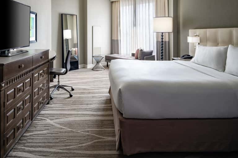 Modern hotel bedroom with king bed, TV, work desk, and floor-to-ceiling windows