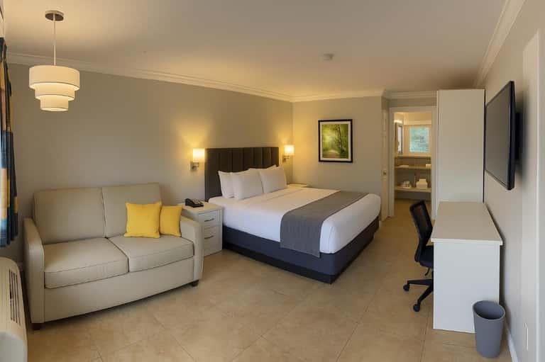 Spacious hotel room with queen bed, sofa, work desk, and bathroom visible