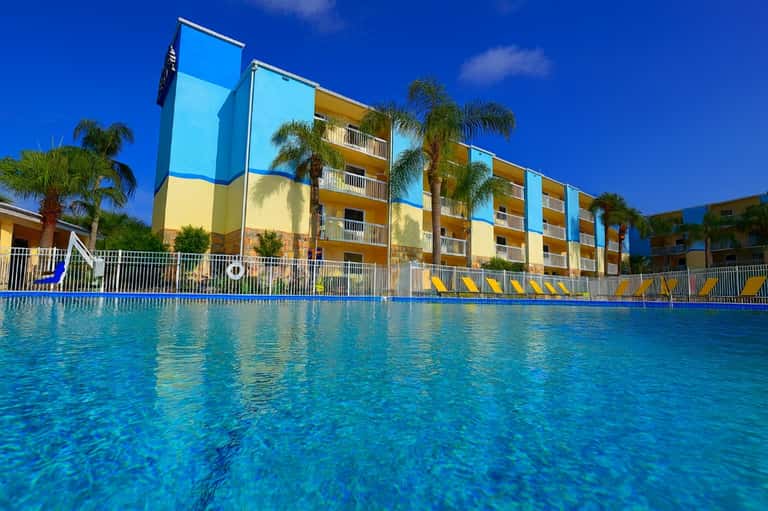 Colorful apartment complex with blue and yellow facade overlooking crystal clear swimming pool under blue sky
