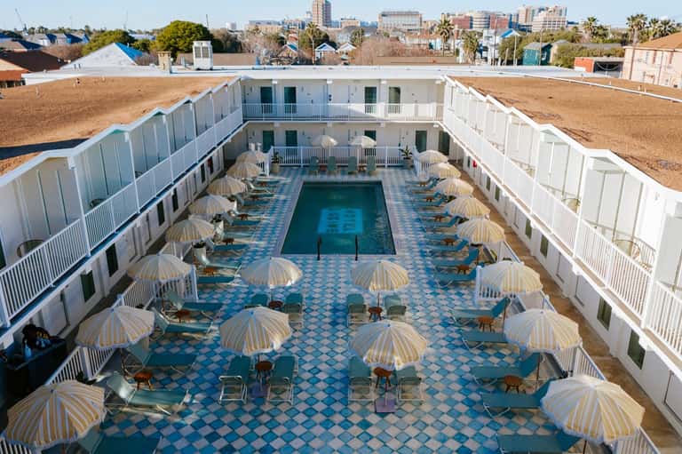 Courtyard-style pool surrounded by white building wings with umbrellas and lounge chairs
