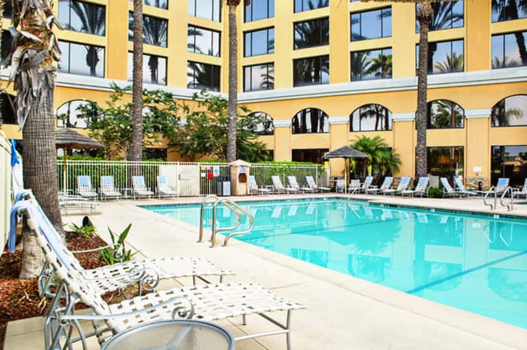 Resort courtyard with turquoise swimming pool, lounge chairs, yellow building facade, and palm trees