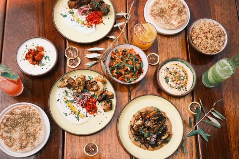 Overhead view of plated Mediterranean dishes with hummus, grilled vegetables, and fresh drinks