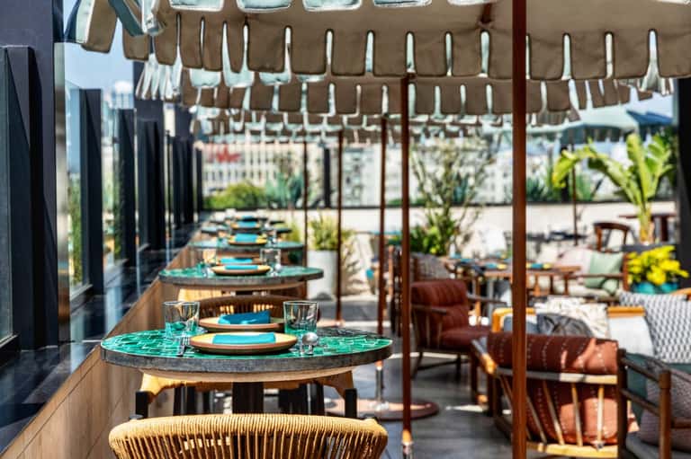 Outdoor dining terrace with turquoise table settings, pergola shade, and palm tree views