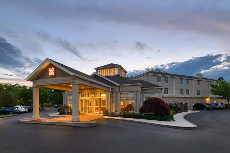 Hotel exterior at dusk with illuminated entrance portico, multi-story building, and parking area