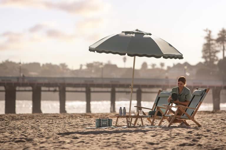 Woman relaxing on beach chair under umbrella near pier and waterfront