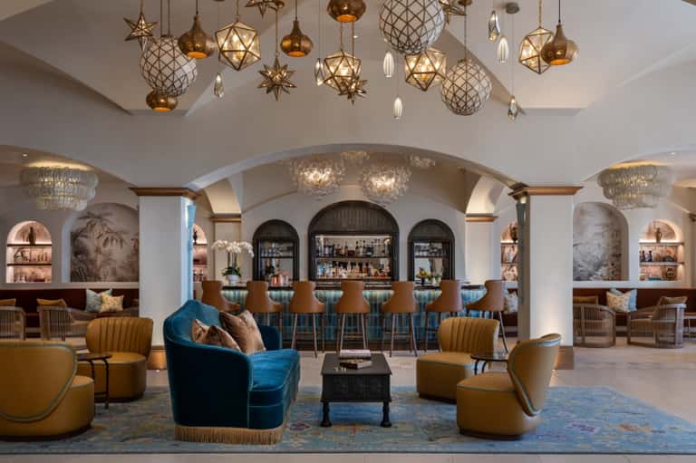 Elegant lobby lounge with ornate gold chandeliers, blue velvet chairs, and arched bar