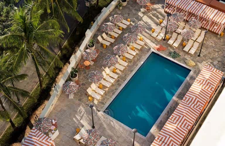 Aerial view of resort pool with striped loungers, umbrellas, and surrounding palm landscaping