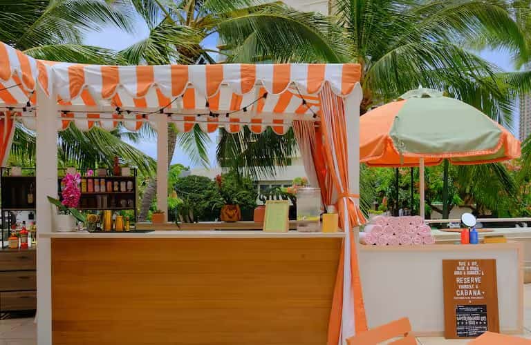 Orange and white striped cabana bar with pink flowers and tropical palm trees