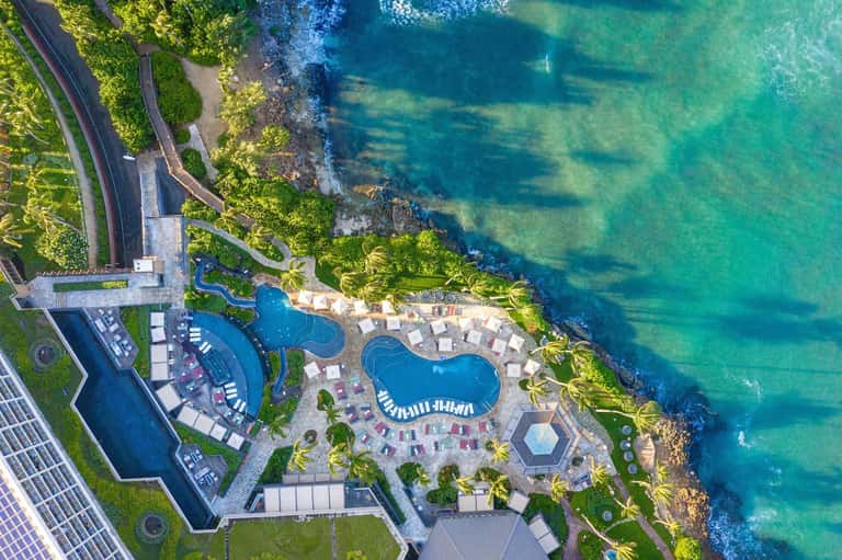 Aerial view of luxury beachfront resort with curved pools, loungers, and turquoise ocean