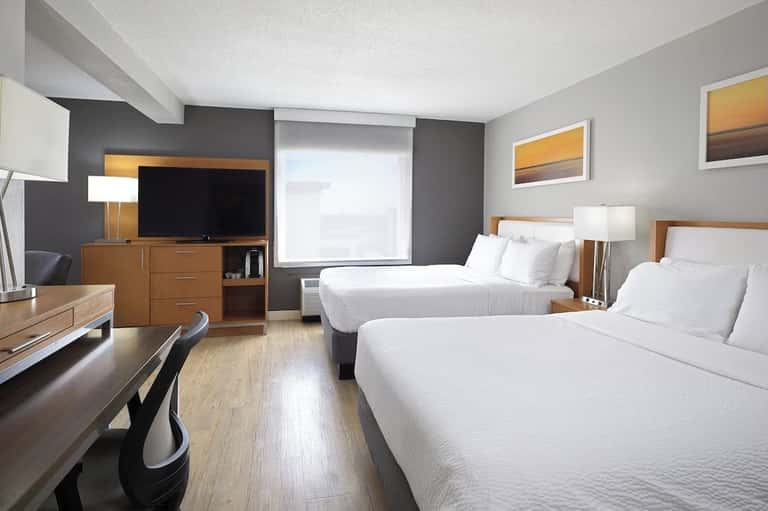 Hotel room with two queen beds, TV, desk, and modern furnishings in neutral tones
