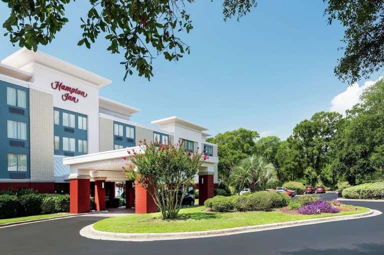 Hampton Inn hotel exterior with white facade, red accents, and landscaped entrance