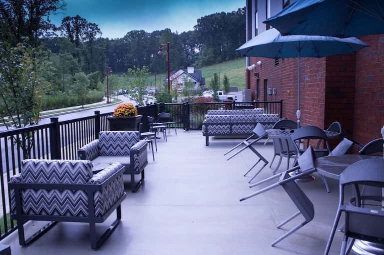 Outdoor terrace with patio furniture, blue umbrella, black railings, and scenic hillside views