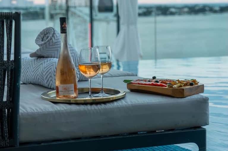 Rosé wine and charcuterie board on lounge by infinity pool overlooking water