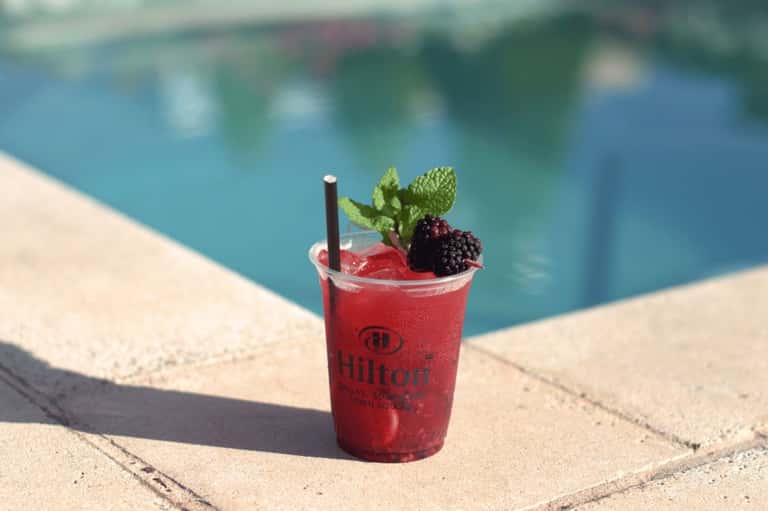 Vibrant red berry cocktail with mint garnish at poolside, branded Hilton cup