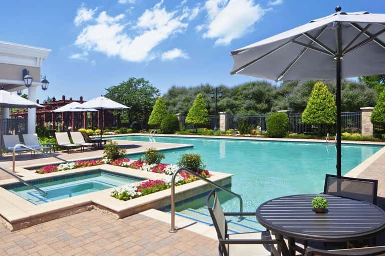 Resort pool area with blue water, lounge chairs, umbrellas, hot tub, and manicured landscaping