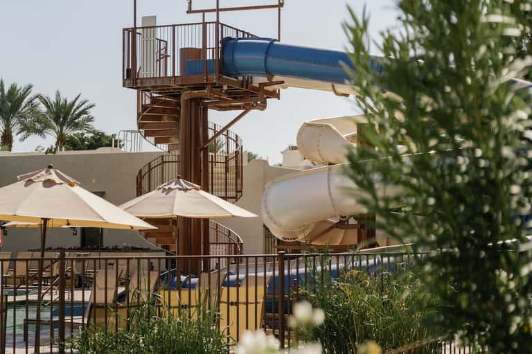 Spiral staircase water slide tower with white tube slides and lounge chairs on pool deck