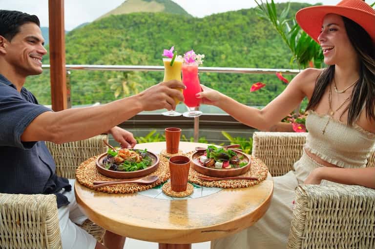 Couple toasting tropical cocktails on a terrace overlooking lush green mountains