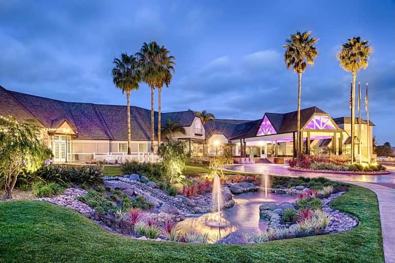 Illuminated modern chapel and event venue at dusk with palm trees and manicured landscaping