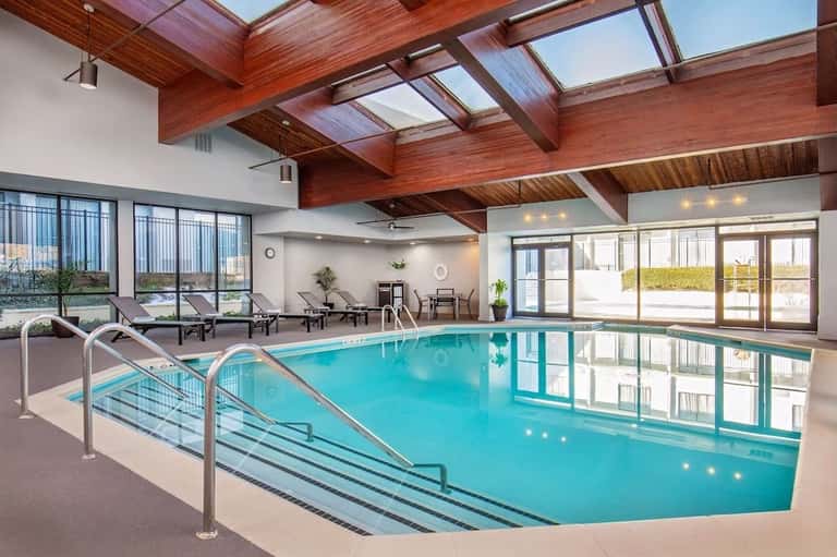 Indoor hotel pool with turquoise water, wooden beam ceiling, skylights, and seating area views
