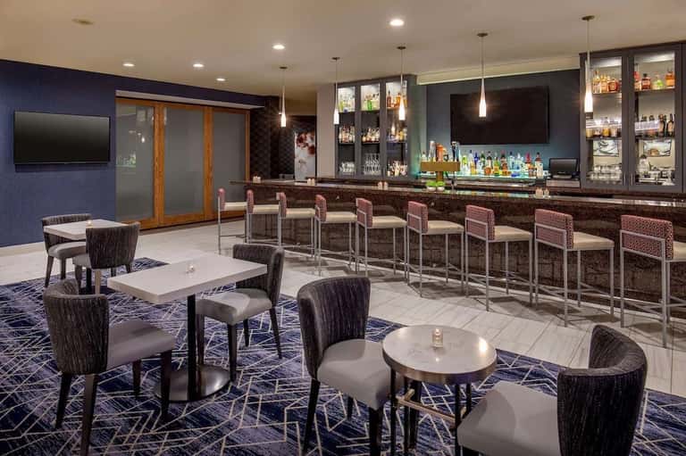 Modern hotel bar lounge with navy walls, upholstered seating, and bar counter with pendant lighting