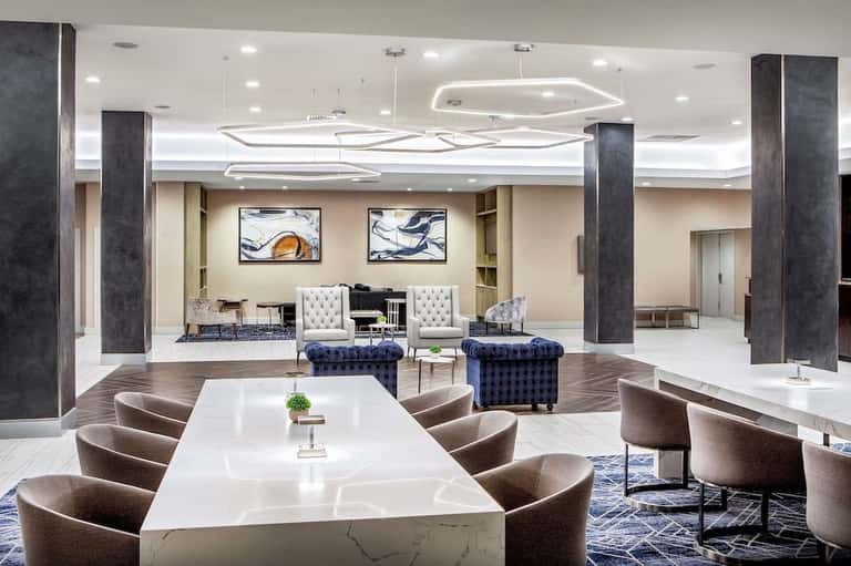 Modern hotel lobby with white marble table, contemporary seating, dark columns, and artistic ceiling lighting