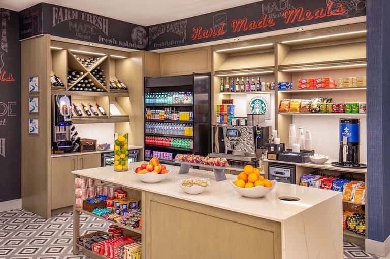 Hotel market shop with illuminated shelving displaying beverages, snacks, wine, and grab-and-go items