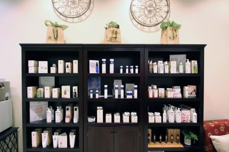 Black shelving unit displaying skincare and beauty products with decorative woven baskets and plants on top