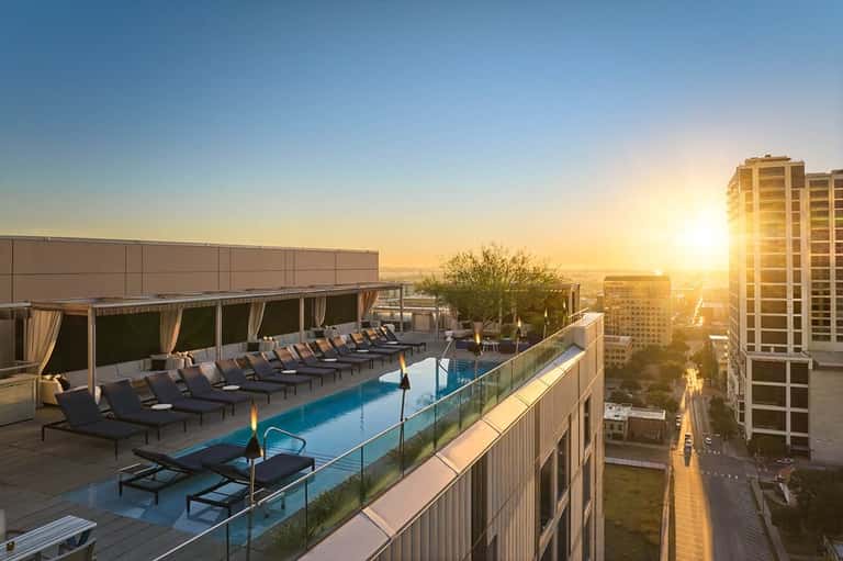 Rooftop pool with lounge chairs at sunset overlooking city and buildings