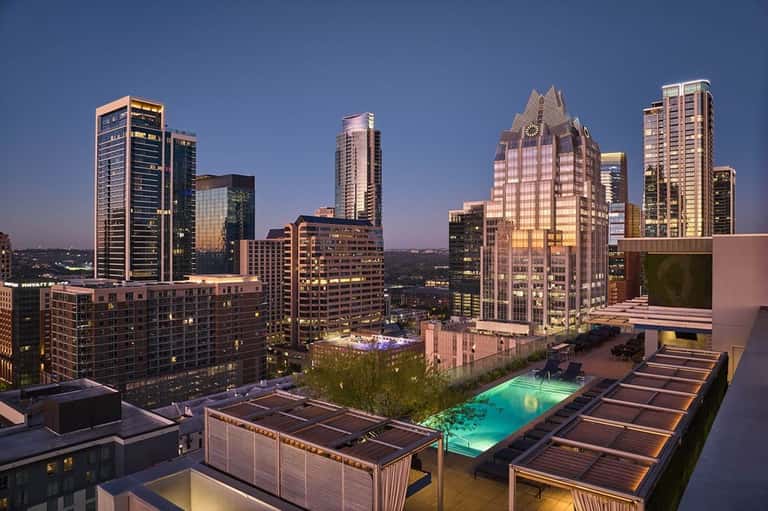 Downtown rooftop pool at dusk with illuminated cityscape and modern buildings